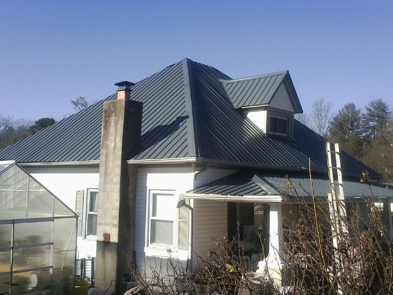 Dark blue standing seam metal roof on a white farmhouse with dormer — Slate & Tile Roof Repair by Roofing Brothers in Crossville