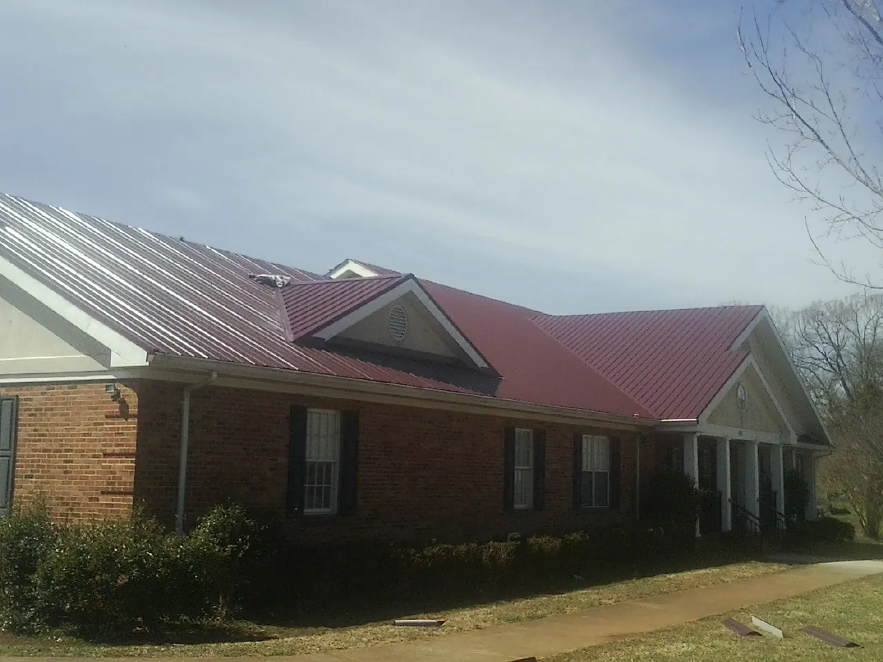 Red metal roof with gabled entries on a long brick building, from a Hail Damage Roof Repair job in Crossville