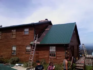 Green metal roof going on a two story log home with ladders set in Crossville