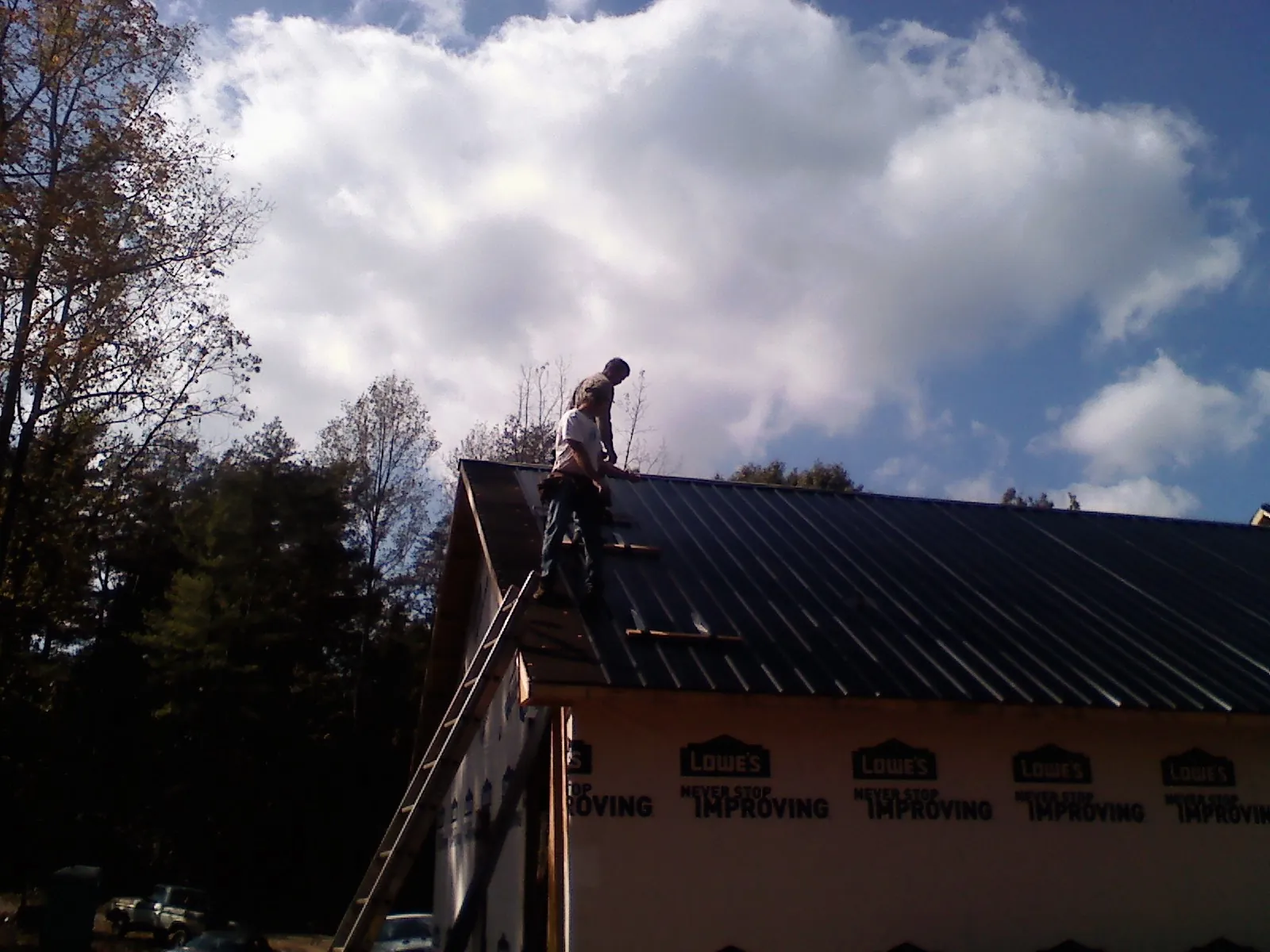 Roofer fastening dark metal panels high against a cloudy sky, from a Roof Inspection job in Crossville