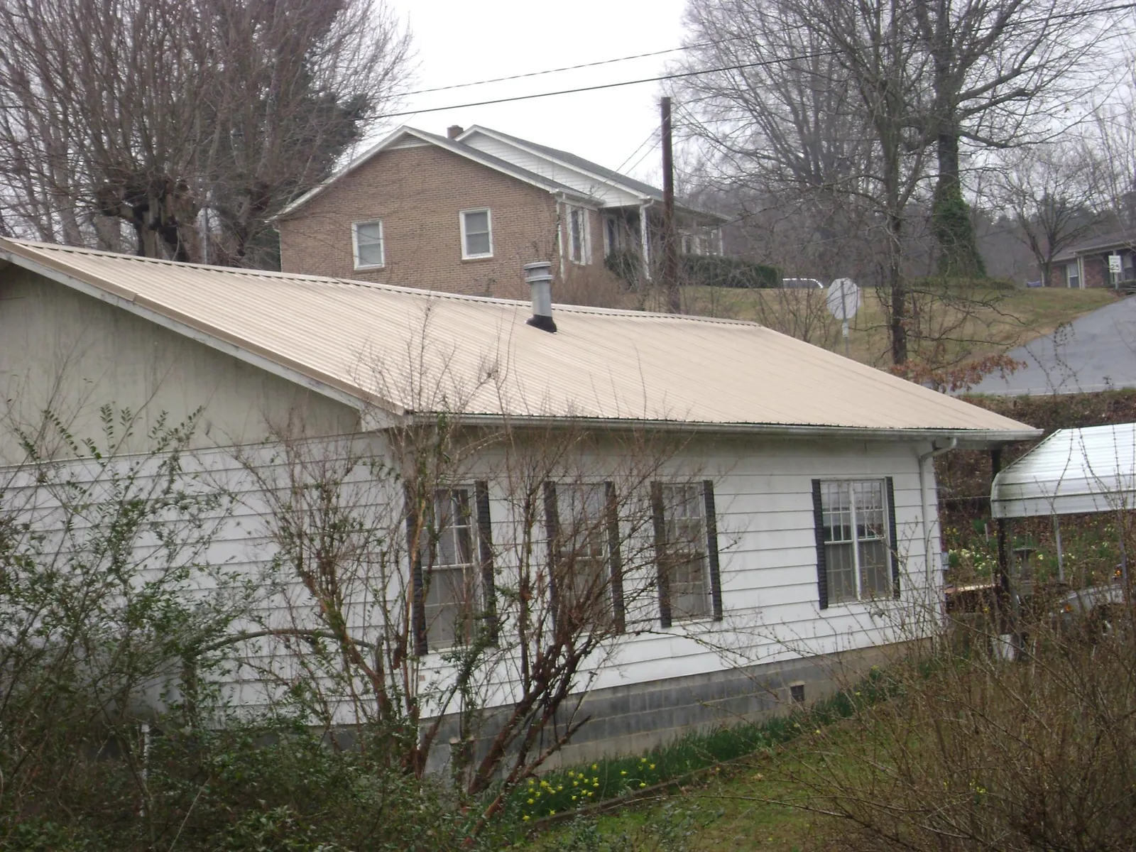 Tan metal roof on a white sided house set into a hillside — Commercial Roofing by Roofing Brothers in Crossville